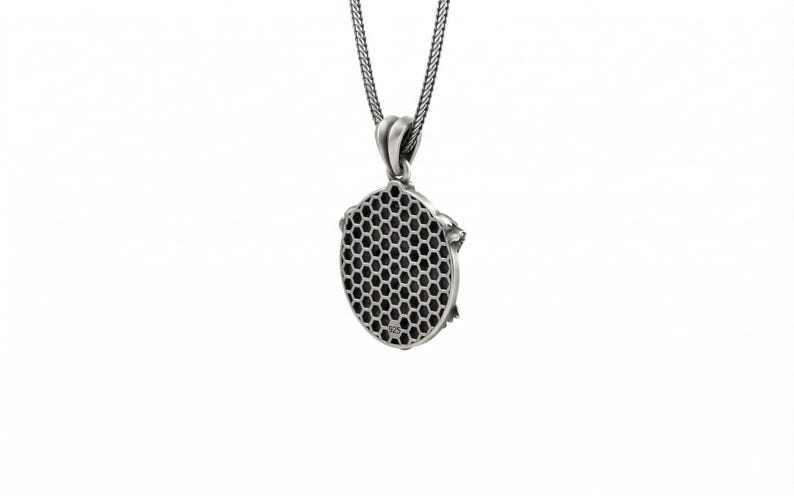May include: A silver pendant necklace with a honeycomb design. The pendant is oval-shaped with a detailed honeycomb pattern in the center. The necklace has a delicate chain and a simple bail. The pendant is made of a shiny, silver-colored metal.