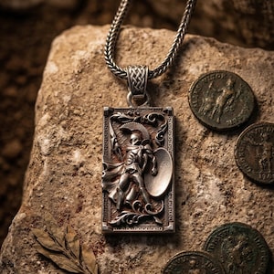 May include: A silver pendant necklace depicting a warrior with a shield and spear in relief. The pendant is suspended from a braided chain. Ancient coins are placed around the pendant on a stone surface. The necklace is a piece of jewellery.