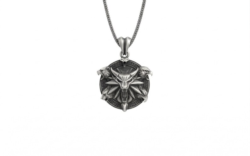 May include: Silver-toned pendant necklace featuring a circular pendant with a central wolf head design, surrounded by three animal heads. The pendant hangs from a delicate chain. The necklace is set against a white background.