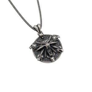 May include: Silver-toned pendant necklace featuring a circular pendant with a detailed, stylized wolf's head and other animal figures. The pendant is suspended from a matching chain. The design has a fantasy or medieval theme.