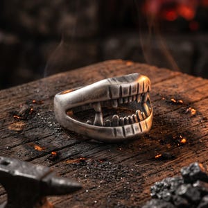 May include: A silver-toned metal ring shaped like an open mouth with visible teeth and fangs. The ring has a weathered, dark finish with detailed carvings of upper and lower teeth, creating a realistic dental structure within the circular band.
