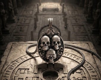 May include: Silver pendant necklace featuring three skulls within an oval frame. The pendant hangs from a braided chain, resting on a stone surface with carved symbols. The background shows an ancient, dimly lit hall.
