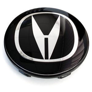 May include: A black and silver car wheel center cap. The cap features a glossy black finish with a silver border and a stylized white and silver emblem in the center. The emblem is a combination of a letter "M" and a vertical line.