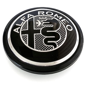 May include: A black and silver Alfa Romeo emblem. The emblem is circular with the words "ALFA ROMEO" in silver lettering around the outer edge. The center features a silver cross and a serpent design.