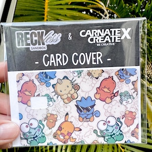 May include: A clear plastic card cover with a vibrant pattern of cartoon characters. The card cover has the text "RECKLESS & CARNATE X CREATE - CARD COVER -" printed on it. The card cover is held in a person's hand.