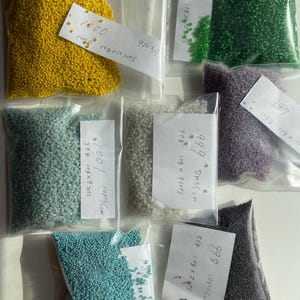 Puede incluir: Surtido de pequeñas cuentas de colores en bolsas de plástico transparente. Los colores incluyen amarillo, verde, morado, azul y gris. Cada bolsa tiene una etiqueta con números y medidas. Ideal para la creación de joyas o proyectos de artesanía.