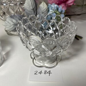 May include: A clear, diamond-cut glass bowl with a scalloped rim and a pedestal base. The bowl has a textured, geometric pattern. A small white tag with the number "2484" is visible.