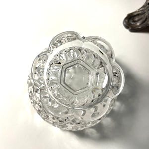 May include: Clear, cut-glass bowl with a scalloped edge and a geometric pattern. The bowl's base has a hexagonal shape. The bowl is likely part of a decorative or serving set.