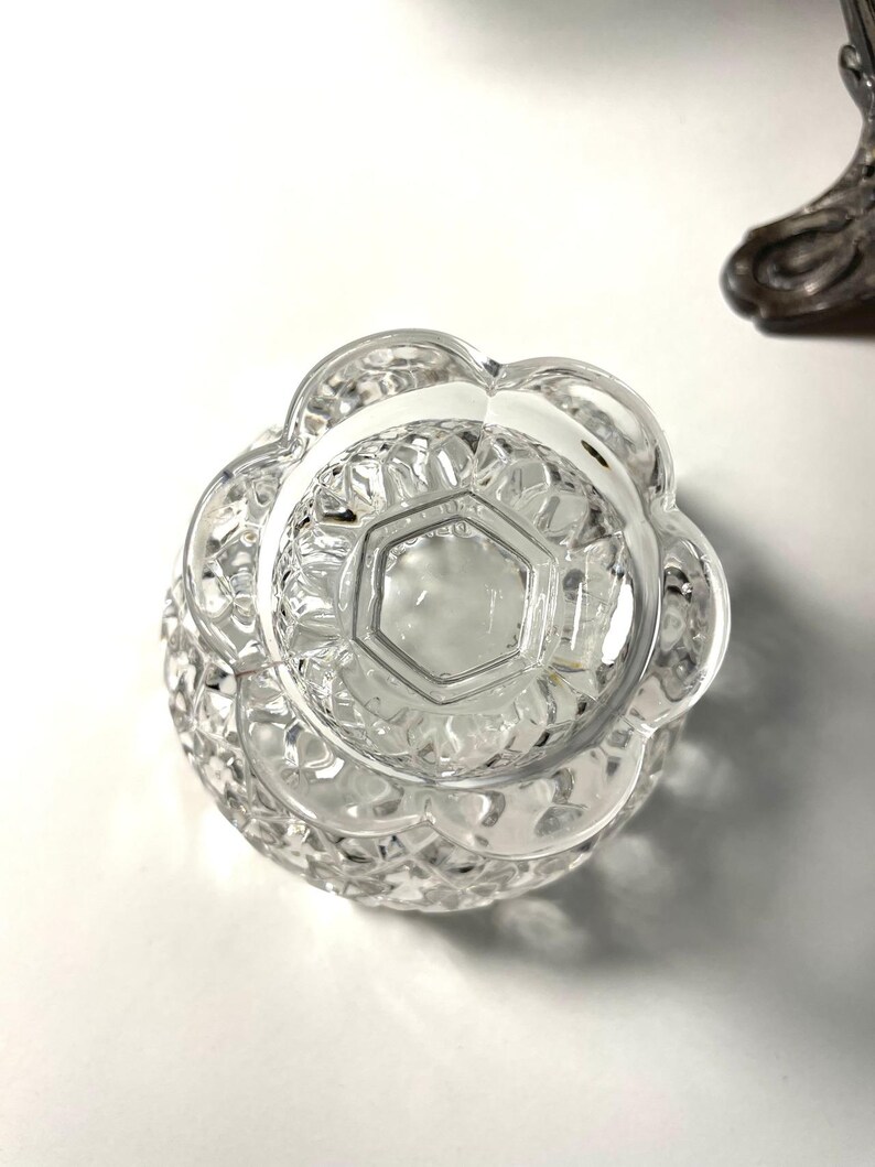 May include: Clear, cut-glass bowl with a scalloped edge and a geometric pattern. The bowl's base has a hexagonal shape. The bowl is likely part of a decorative or serving set.