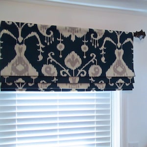 May include: A blue and white patterned roman shade with a valance. The shade is made of a fabric with a geometric design. The valance is a decorative piece that covers the top of the shade.
