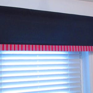 May include: A navy blue window valance with a red and white striped border. The valance is mounted above a white window with horizontal blinds. The rod is dark brown.