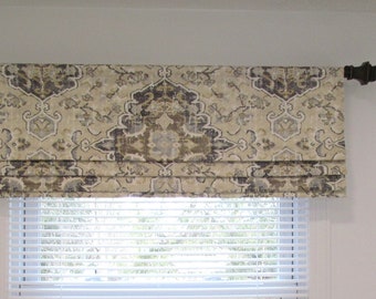 May include: A beige roman shade with a brown and gray patterned design. The shade is mounted above a white window blind.