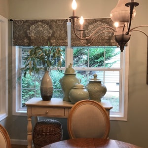 May include: A dining room with a light green wall, two windows with brown patterned valances, a wooden table with two chairs, and a white side table with three decorative ceramic vases in shades of blue and green.
