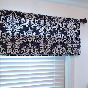 May include: A navy blue and white damask patterned roman shade with white trim. The shade is mounted above a white window blind.