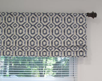 May include: A roman shade window treatment with a geometric pattern in shades of blue and cream. The shade is mounted on a brown metal rod.