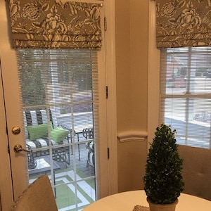 May include: A white door with a window and a patterned valance. The window has white blinds and looks out onto a patio with furniture. A small green topiary plant sits on a table in the foreground.