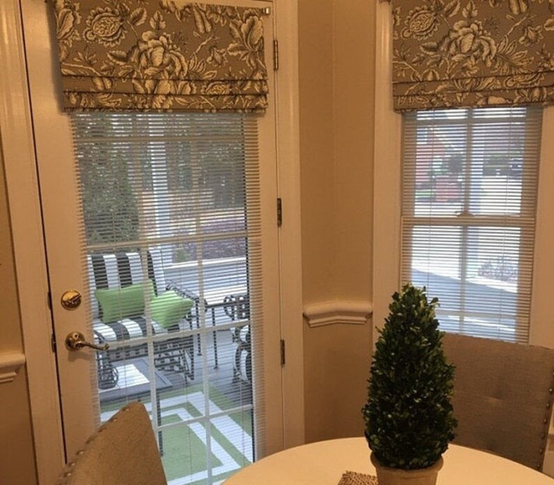 May include: A white door with a window and a patterned valance. The window has white blinds and looks out onto a patio with furniture. A small green topiary plant sits on a table in the foreground.