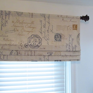 May include: A beige roman shade with a vintage Parisian theme. The fabric features a repeating pattern of black text and stamps, including "Postes Francaises" and "Paris, France".