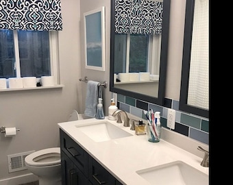 May include: A white bathroom vanity with two sinks, a white toilet, and a mirror with a blue and white patterned valance. The vanity has dark blue cabinets and brushed nickel hardware.