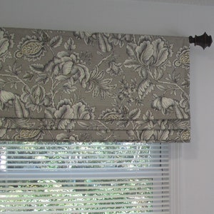 May include: A gray and white floral patterned roman shade with a brown metal rod. The shade is pulled up to reveal a white window blind.