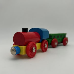 May include: A colorful wooden toy train with a red engine, blue roof, and yellow base. The train has red wheels and a green cargo car. The train's front has a silver-colored bumper. A classic toy for children.