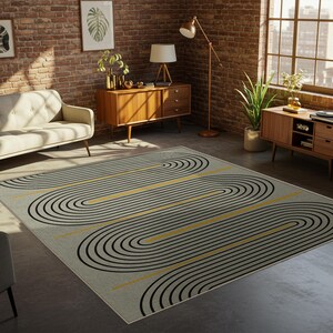 Könnte beinhalten: Ein rechteckiger Teppich mit geometrischem Muster. Der Teppich hat einen hellgrauen Hintergrund mit schwarzen und gelben geschwungenen Linien. Die Linien bilden ein sich wiederholendes Design über den Teppich. Der Teppich liegt auf einem Betonboden.
