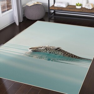 May include: A rectangular area rug featuring a serene image of a leopard swimming in light blue water. The leopard's spotted pattern is visible, and the rug has a light blue border.