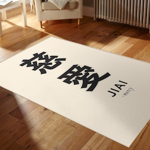 Könnte beinhalten: Rechteckiger cremefarbener Teppich mit großen schwarzen chinesischen Schriftzeichen und dem Wort "JIAI" in Schwarz, darunter "mercy". Der Teppich liegt auf einem Holzboden.