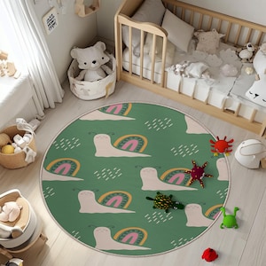 May include: A round, green rug with a whimsical snail and rainbow pattern. The rug features a repeating design of smiling snails with rainbow shells and white rain cloud accents. The rug is surrounded by a white border and is placed in a nursery.