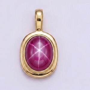 May include: A gold pendant with an oval, star ruby gemstone. The ruby is a deep pink color with a six-ray star pattern. The pendant has a simple, elegant design.