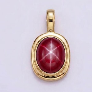 May include: A gold pendant featuring an oval, star-shaped ruby gemstone. The ruby is a deep red colour, and the gold setting has a polished finish. The pendant has a loop at the top for a chain.