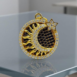 Puede incluir: Un colgante circular de oro con un motivo de sol y luna creciente. El borde exterior y la luna creciente están incrustados con piedras blancas transparentes, mientras que los rayos del sol y el fondo de la luna están llenos de piedras negras.