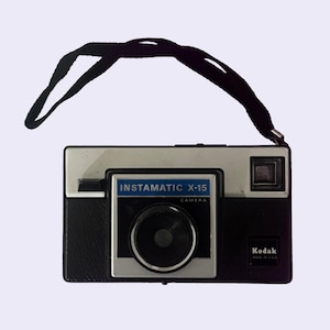 May include: Vintage Kodak Instamatic X-15 camera with a black and silver body and a black strap. The camera has the text "INSTAMATIC X-15 CAMERA" on the front. The camera is marked "Kodak MADE IN U.S.A."