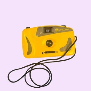 May include: A yellow Lifelong camera with a black strap. The camera has a rectangular shape with a lens and flash. The word "Lifelong" is printed on the top of the camera.