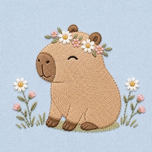 Op de afbeelding: Geborduurd beeld van een lachende capibara met een bloemenkrans, omringd door geborduurde bloemen en gras. De capibara is lichtbruin met donkerbruine accenten. De achtergrond is een lichtblauwe stof.