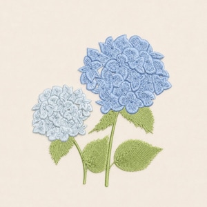 May include: Embroidered image of two hydrangea blooms in shades of light blue, with green stems and leaves. The flowers are detailed with a textured stitch, set against a cream-colored background. The design evokes a floral theme.