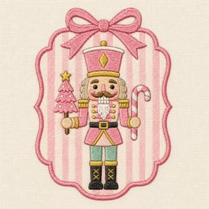 May include: An embroidered nutcracker design featuring a pink uniform, a tall hat, and a white beard. The figure holds a pink Christmas tree and a candy cane. It is framed by a pink striped scalloped border topped with a large pink bow.