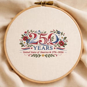 K&ouml;nnte beinhalten: Gesticktes Bild in einem Holzrahmen mit dem Text "250 YEARS" in Rot und Blau, umgeben von Blumen- und Bl&auml;tterdesigns. Darunter steht der Text "United States of America 1776-2026".