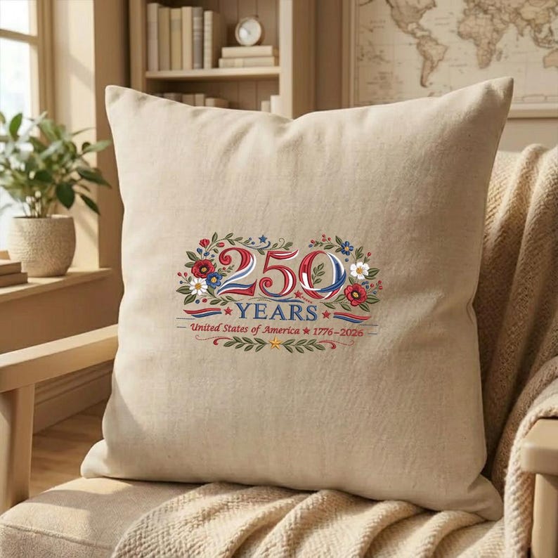 K&ouml;nnte beinhalten: Beiges quadratisches Kissen mit einem farbenfrohen Blumendesign und dem Text "250 YEARS - United States of America 1776-2026". Das Design weist rote, wei&szlig;e und blaue Elemente auf.