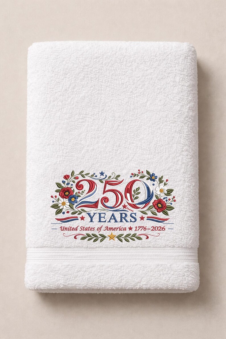 May include: White bath towel with an embroidered design celebrating 250 years of the United States of America. The design includes the numbers "250" in red, white, and blue, surrounded by floral and leaf elements.
