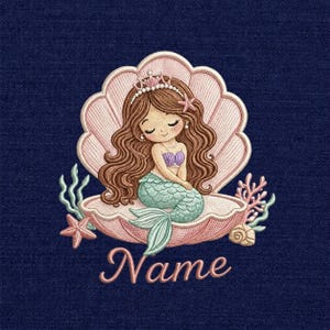 Puede incluir: Diseño bordado de una sirena con cabello castaño largo, una corona y una cola turquesa, sentada en una concha rosa. El diseño incluye una estrella de mar, coral y la palabra "Name" en cursiva sobre un fondo azul marino.