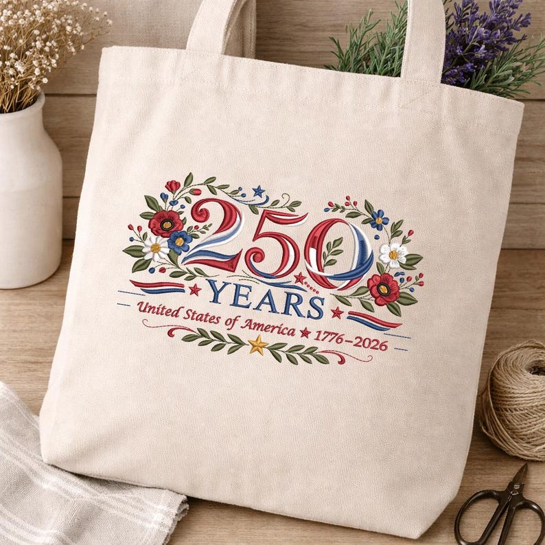 May include: Beige canvas tote bag with embroidered design. The design features the number "250" in red, white, and blue, surrounded by floral elements. Text below reads "YEARS" and "United States of America 1776-2026".