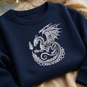 May include: Navy blue sweatshirt featuring a detailed white dragon design. The dragon is depicted with intricate wing and body patterns, holding a flame. The design is centered on the chest, creating a striking visual.