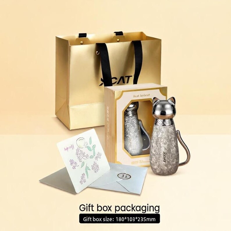 Puede incluir: Una bolsa de regalo dorada con asas negras y la palabra "CAT" impresa. Una botella de agua de acero inoxidable con forma de gato est&aacute; junto a una caja de regalo. Tambi&eacute;n se incluye una tarjeta de felicitaci&oacute;n y un sobre. El tama&ntilde;o de la caja de regalo es de 180*103*235mm.