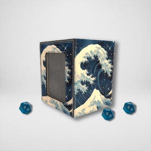 May include: A blue and white dice box featuring a Japanese wave design. The box has a rectangular window and is accompanied by three blue, twenty-sided dice.
