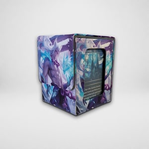 Può includere: Un contenitore quadrato per carte da gioco con un'illustrazione fantasy viola e blu che raffigura un personaggio dai capelli lunghi e una creatura spirituale luminosa. Il pannello frontale presenta un ritaglio rettangolare con una carta da gioco.