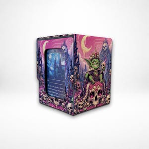 May include: A rectangular card storage box featuring a vibrant pink and purple illustration of a green goblin wearing a crown and sitting on a large skull throne. The box includes a clear window displaying a blue trading card with gothic architecture.