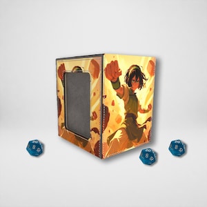Peut inclure: Un coffret à dés carré de couleur beige avec un cadre noir et une découpe, orné d'une illustration de style anime d'un personnage en position de combat. Trois dés bleus à vingt faces sont disposés autour du coffret.