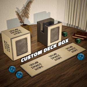 Op de afbeelding: Aangepaste deckboxen met de tekst "YOUR IMAGE HERE" en "CUSTOM DECK BOX". De dozen zijn beige met een donkerbruin frame. De afbeelding toont ook blauwe en groene dobbelstenen en een beige speelmat.