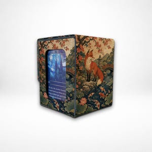 May include: A rectangular card storage box featuring a printed scene of a fox standing on a rock near a stream with koi fish, lotus flowers, and a bridge. A central window displays a blue trading card with text and a stained glass illustration.